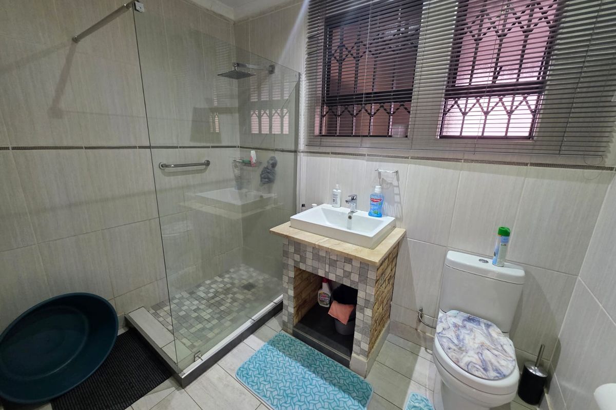 A functional bathroom featuring a glass-enclosed walk-in shower, a modern vessel sink vanity, and a standard toilet with tiled walls and flooring.