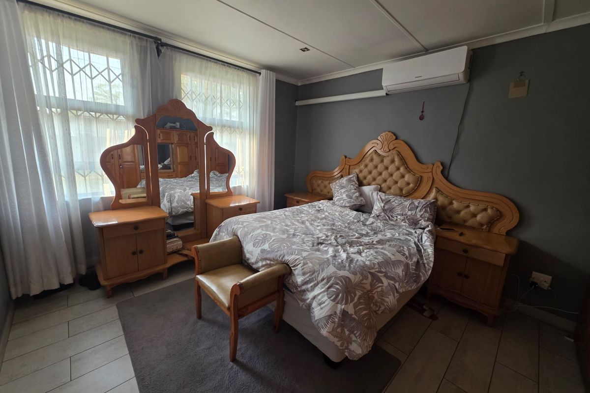 Spacious bedroom featuring tiled flooring, a wall-mounted air conditioning unit, and large windows with security bars.