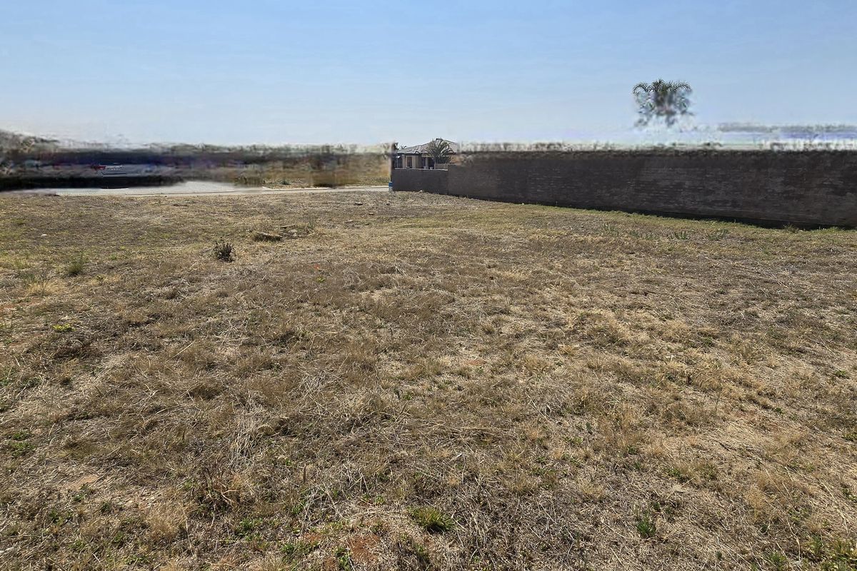 A vacant residential plot featuring perimeter brick boundary walls and open, undeveloped land with natural ground cover.