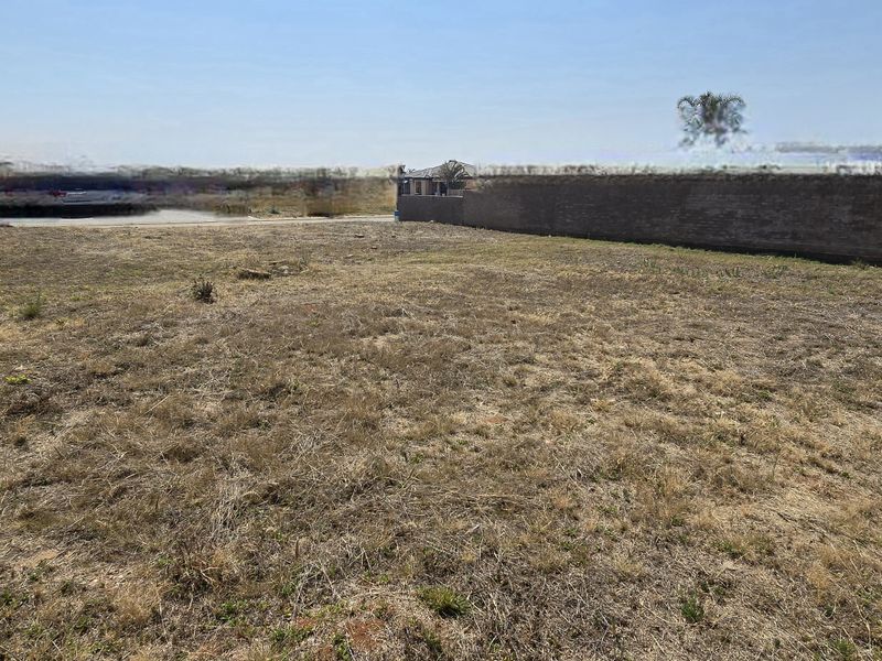 A vacant residential plot featuring perimeter brick boundary walls and open, undeveloped land with natural ground cover.