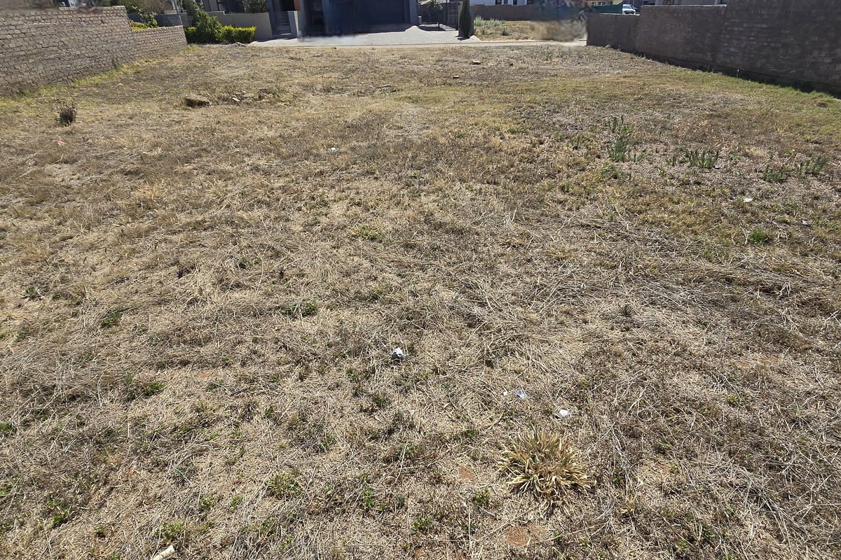 A vacant residential plot featuring perimeter brick boundary walls and dry, unmaintained grass, offering a blank canvas for future development.