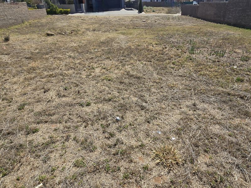 A vacant residential plot featuring perimeter brick boundary walls and dry, unmaintained grass, offering a blank canvas for future development.
