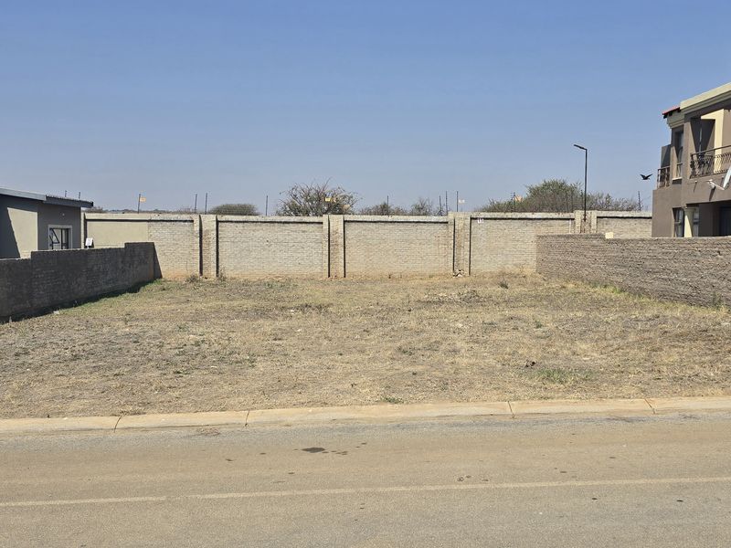 A vacant residential plot situated between existing properties, featuring perimeter boundary walls and street-level access.