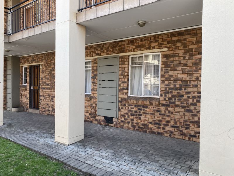 A ground-level paved patio area featuring exposed brickwork, concrete support pillars, and secure access points to the townhouse unit.