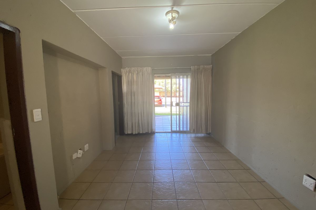 An empty living room featuring tiled flooring and a sliding glass door with a security gate, providing direct access to the outdoor area.