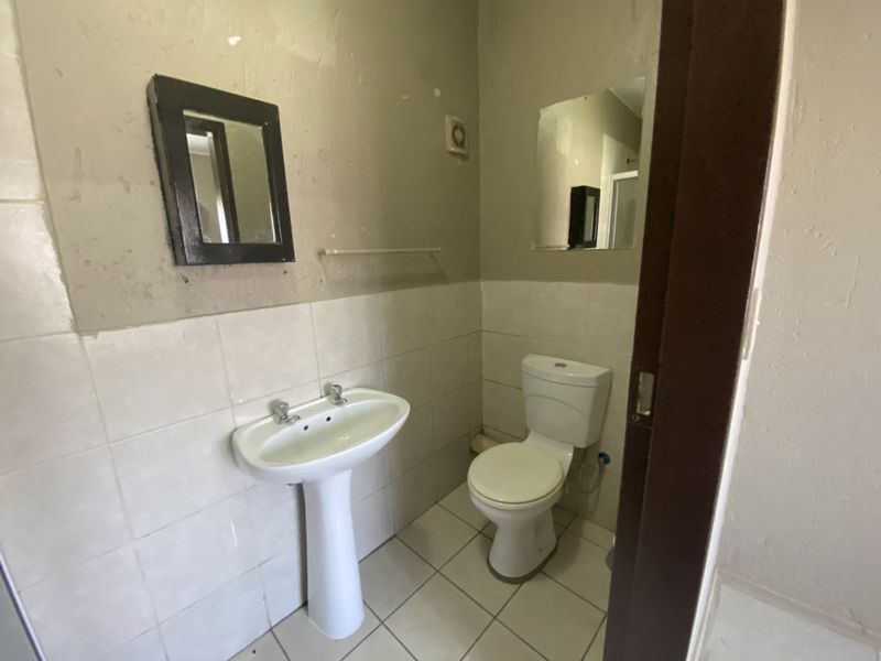 A compact guest bathroom featuring a pedestal basin, toilet, and tiled flooring, currently requiring cosmetic updates to the wall finishes.