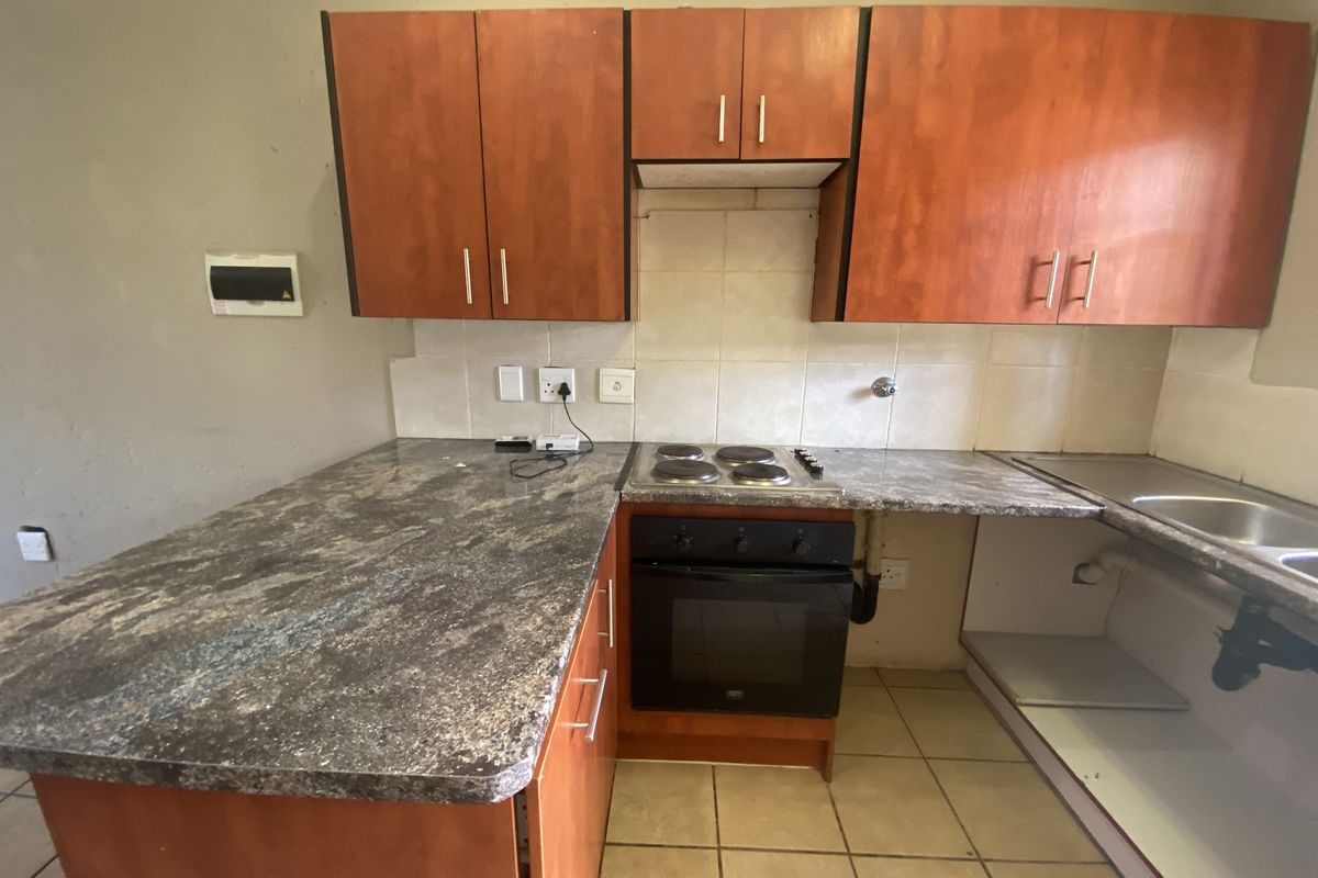A dated kitchen featuring wood-look cabinetry, laminate countertops, a built-in oven and hob, and tiled flooring, currently requiring cosmetic updates and repairs.