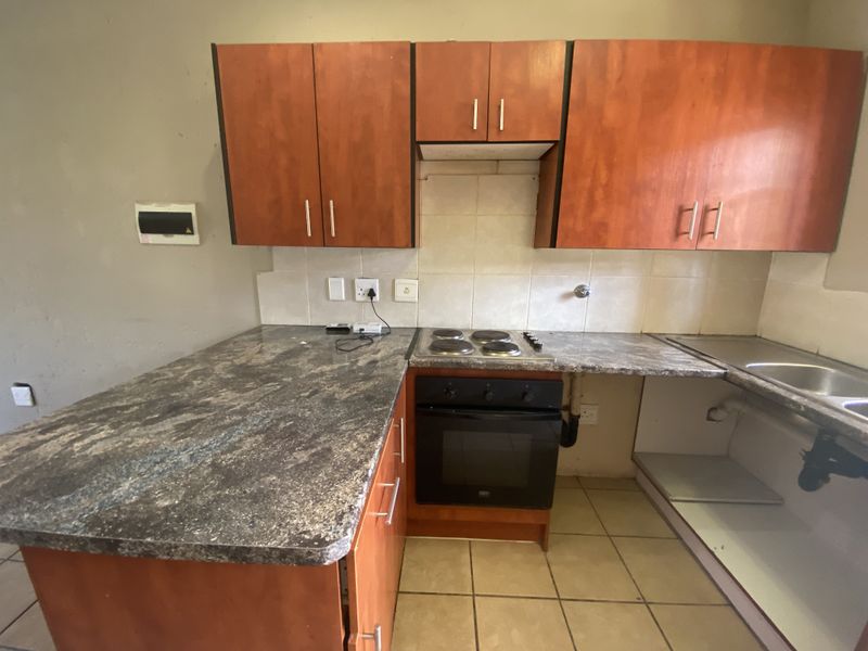 A dated kitchen featuring wood-look cabinetry, laminate countertops, a built-in oven and hob, and tiled flooring, currently requiring cosmetic updates and repairs.