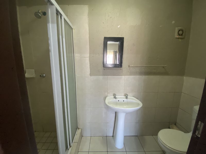 A functional bathroom featuring a pedestal basin, shower enclosure, and toilet, with tiled finishes and an extractor fan. The space requires cosmetic updates.