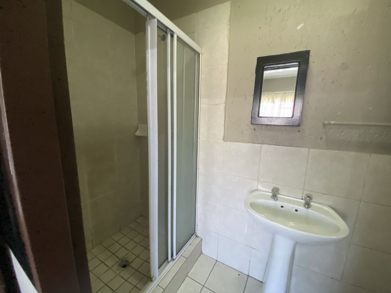 A dated bathroom featuring a shower enclosure and a pedestal basin, requiring cosmetic updates to the wall finishes and tiling.