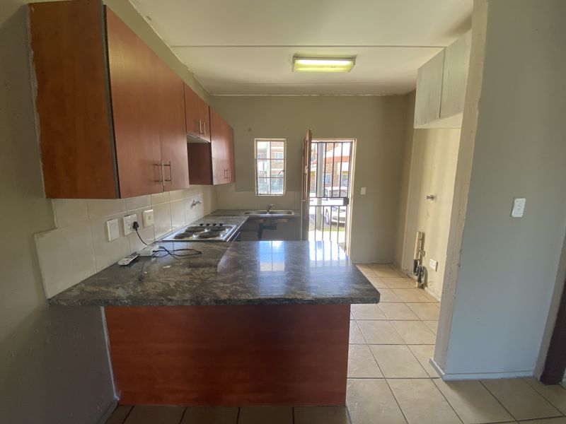 A functional kitchen featuring built-in cabinetry, a breakfast counter, electric hob, and direct access to the exterior via a security gate.