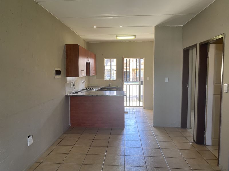 Open-plan living area featuring a compact kitchen with built-in cabinetry, granite countertops, and tiled flooring, leading to an exterior security gate.