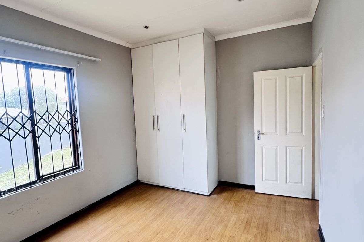A bright, empty bedroom featuring wood-look laminate flooring, built-in white cabinetry, and security bars on the window.