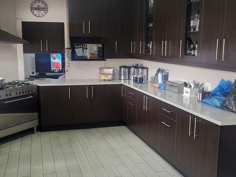 A functional kitchen featuring dark wood cabinetry, stone countertops, a gas stove with extractor fan, and light-toned tiled flooring.