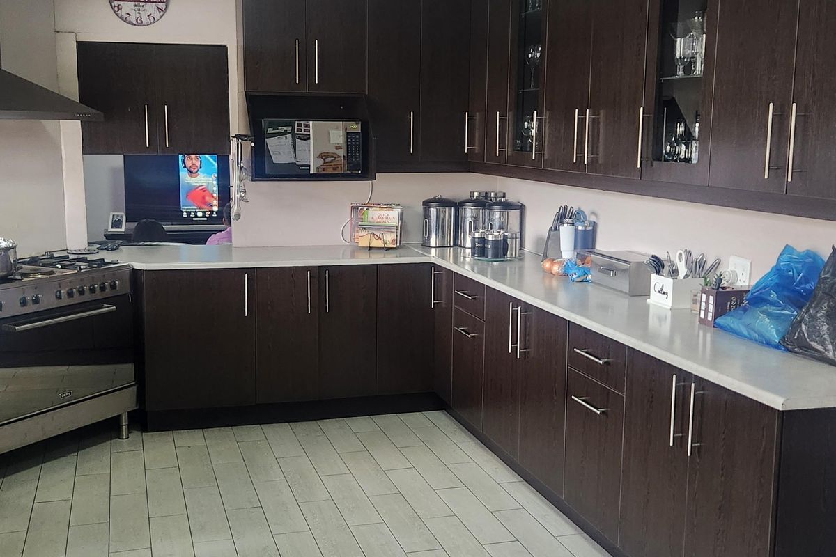 A functional kitchen featuring dark wood cabinetry, stone countertops, a gas stove with extractor fan, and light-toned tiled flooring.