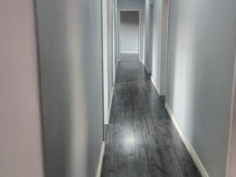 A clean, well-lit hallway featuring dark wood-look laminate flooring and multiple recessed ceiling lights, providing access to various rooms.