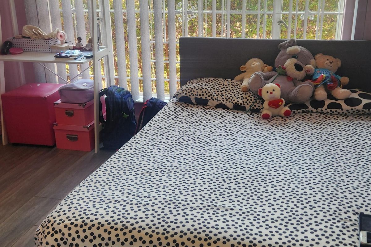 A bedroom featuring laminate flooring and large windows fitted with vertical blinds and security bars.