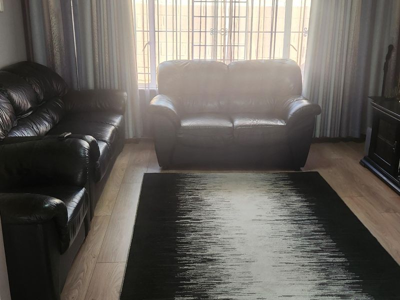A living room featuring light-toned laminate flooring and a timber-paneled ceiling, with large windows fitted with security bars.