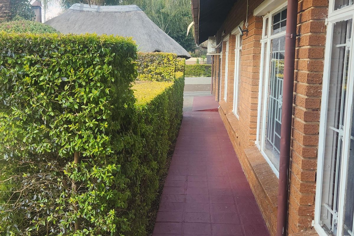 A side walkway featuring a painted tiled path, brick exterior walls, and established garden hedging alongside the property.