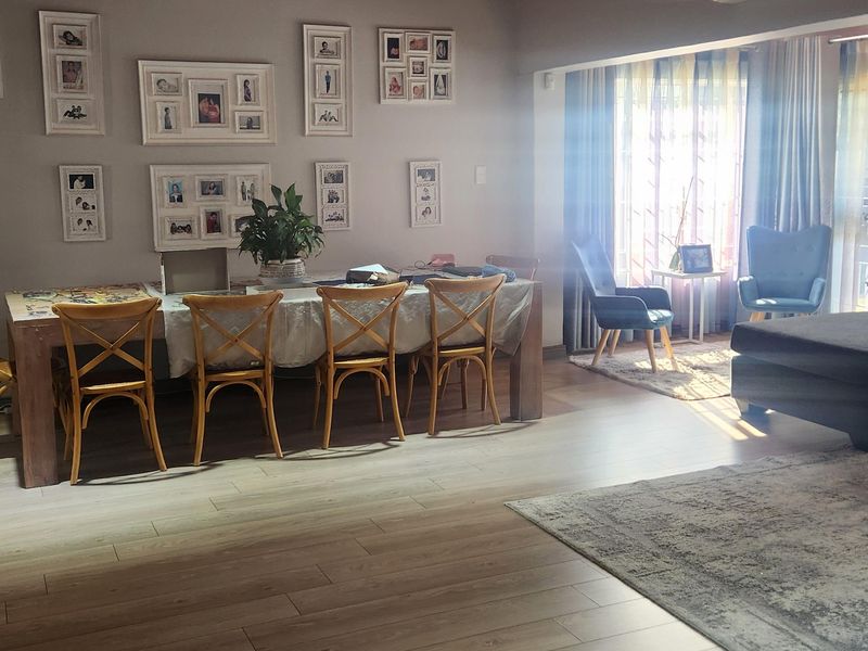 Spacious open-plan living and dining area featuring modern laminate flooring, a warm timber-paneled ceiling, and a wall-mounted split system air conditioner.