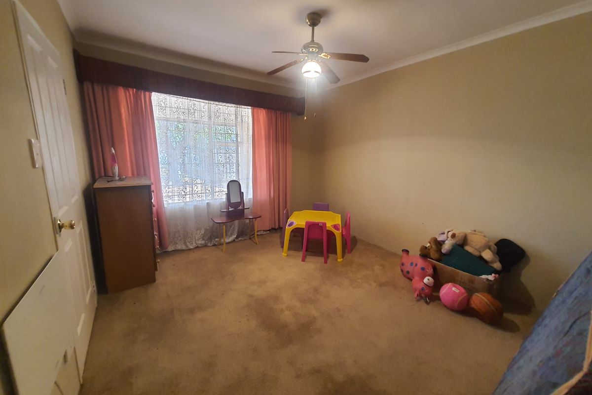 A bedroom featuring a ceiling fan and large window with curtain pelmet, finished with wall-to-wall carpeting.