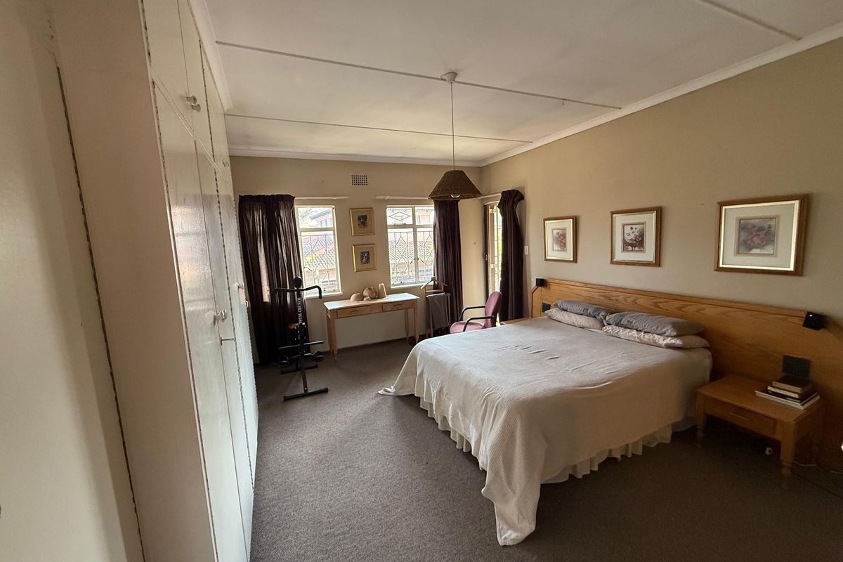 Spacious bedroom featuring built-in cupboards, large windows with security bars, and a neutral color palette.