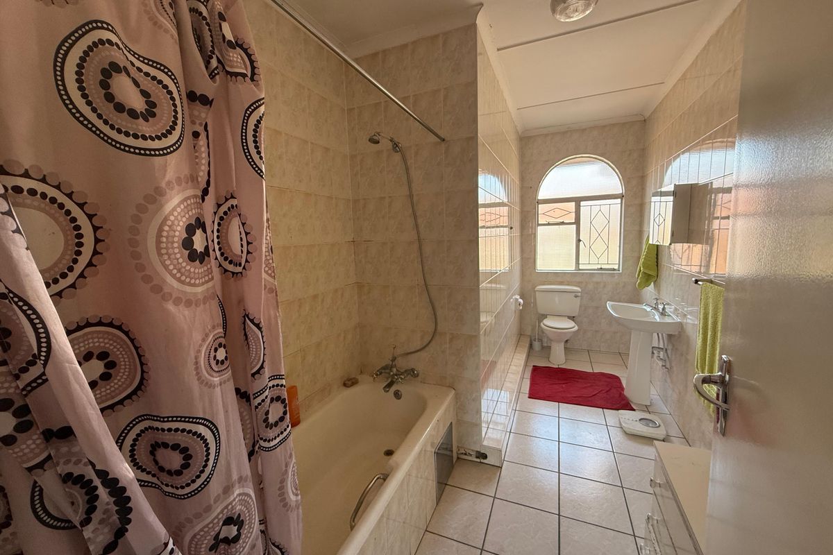 A functional bathroom featuring a bathtub with shower attachment, pedestal basin, and toilet, finished with neutral wall and floor tiling.