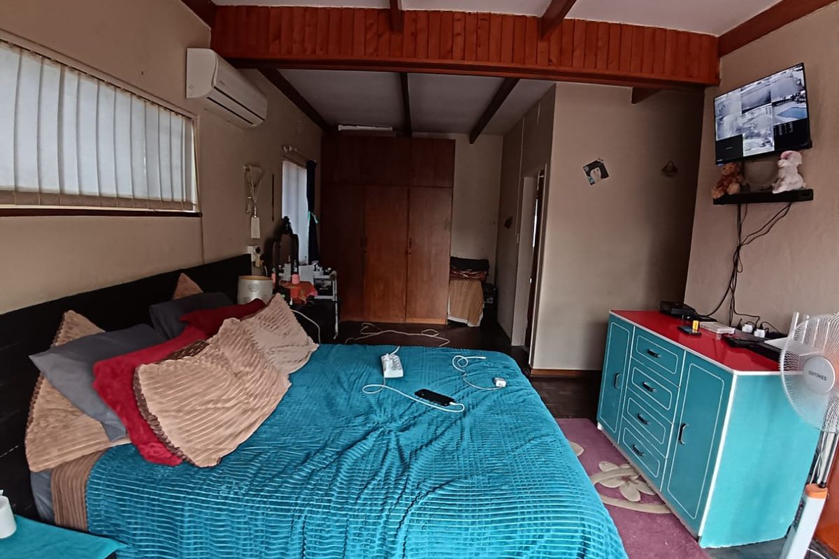 Spacious bedroom featuring exposed timber ceiling beams, built-in wooden cabinetry, and a wall-mounted air conditioning unit.