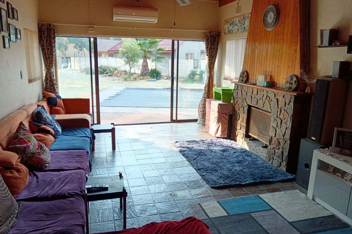Spacious living room featuring a stone fireplace, exposed timber ceiling, and large sliding glass doors providing direct access to the rear garden and pool area.