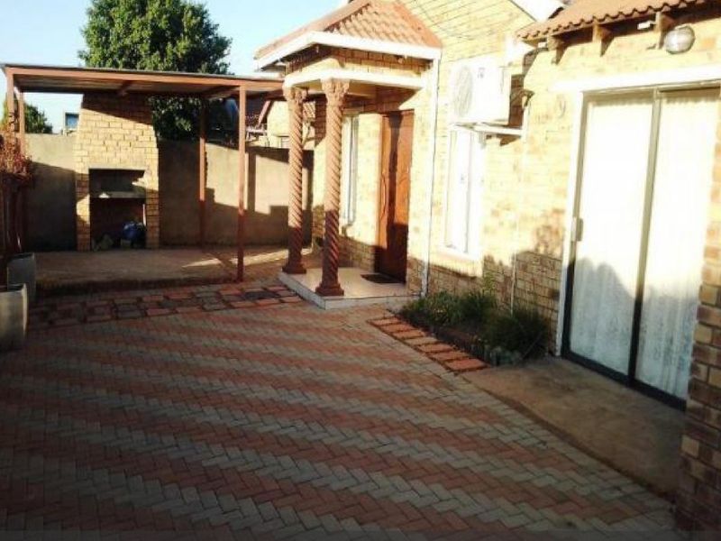 A paved rear courtyard featuring a covered patio area with a built-in brick braai, accessible via sliding glass doors.