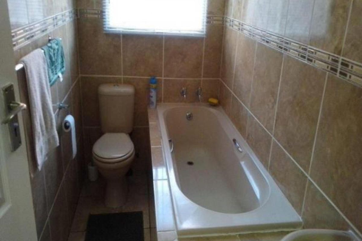 A compact bathroom featuring full-height wall tiling, a built-in bathtub, and a standard toilet.