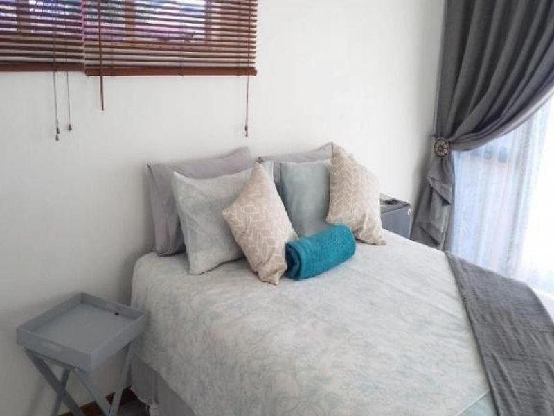 A bedroom featuring neutral walls, window blinds, and floor-to-ceiling curtains, providing a simple and functional sleeping space.