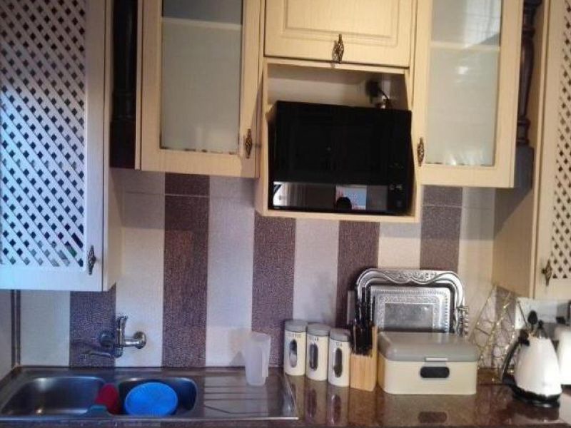 A kitchen prep area featuring built-in cabinetry, a stainless steel sink, and a built-in microwave unit with decorative glass-fronted cupboards.