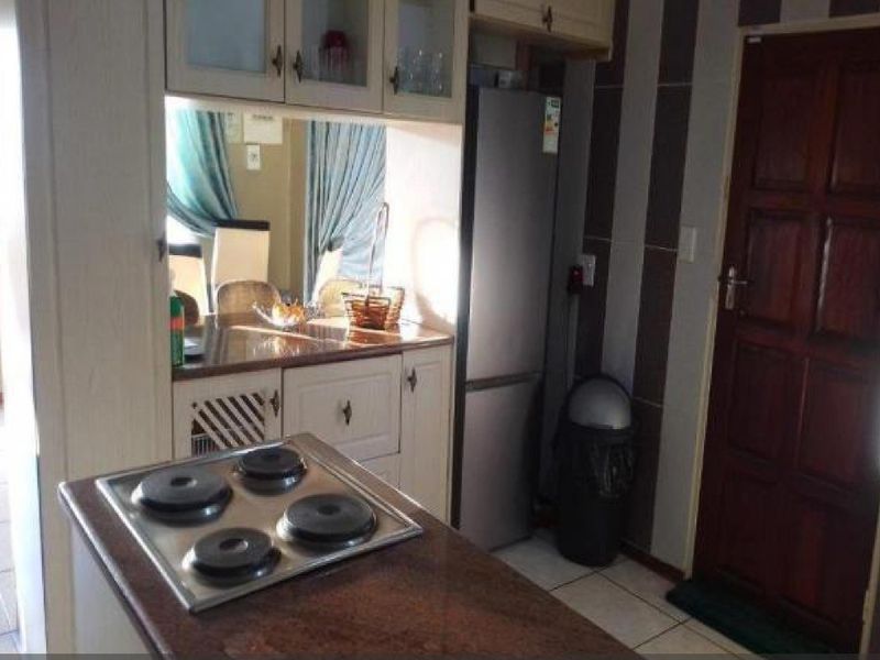 A compact kitchen area featuring a built-in hob on a stone-topped island, overhead cabinetry, and tiled flooring.