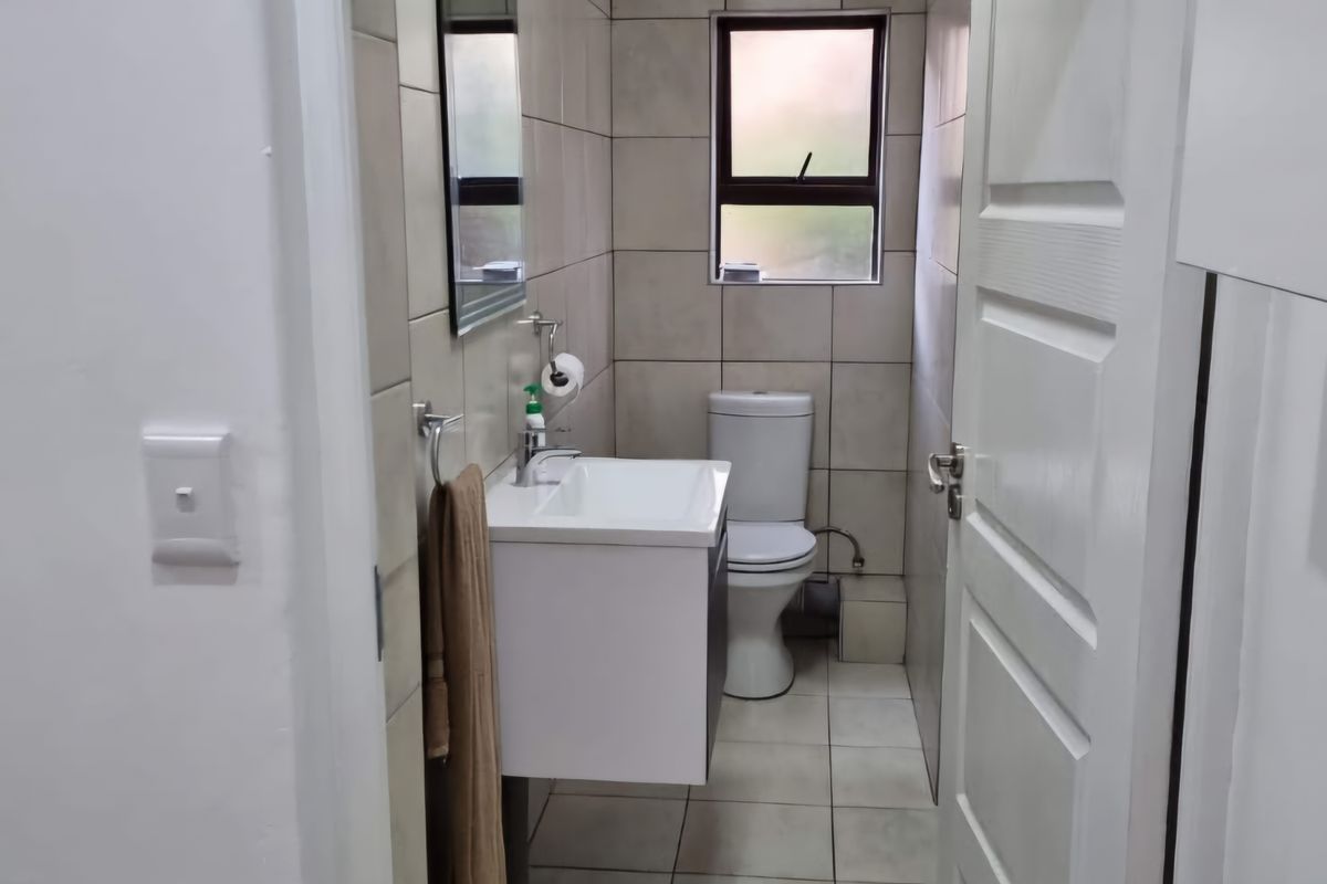 A compact guest bathroom featuring a wall-mounted vanity, ceramic toilet, tiled walls and flooring, and an integrated extractor fan.