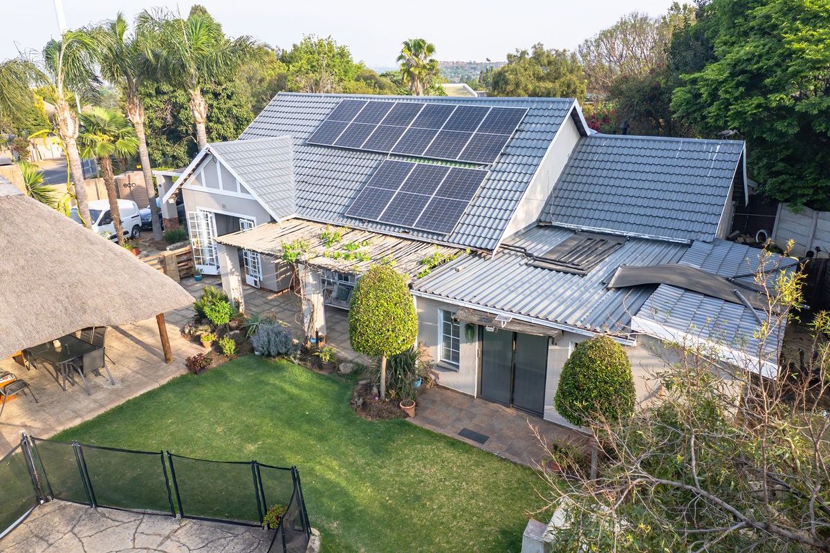 Aerial view of the property featuring a tiled roof with solar panels, a spacious garden, paved patio area, and a thatched lapa.