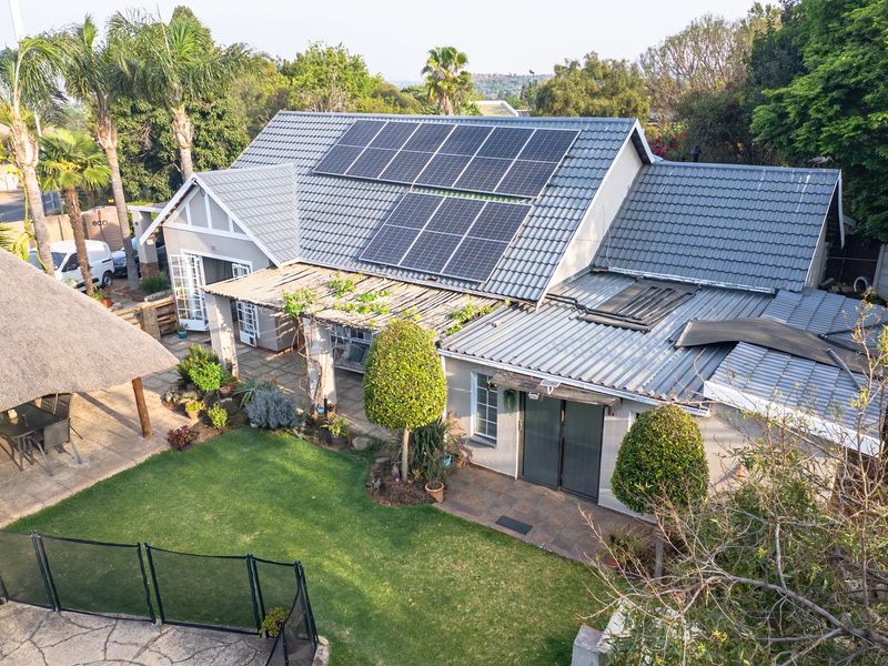 Aerial view of the property featuring a tiled roof with solar panels, a spacious garden, paved patio area, and a thatched lapa.