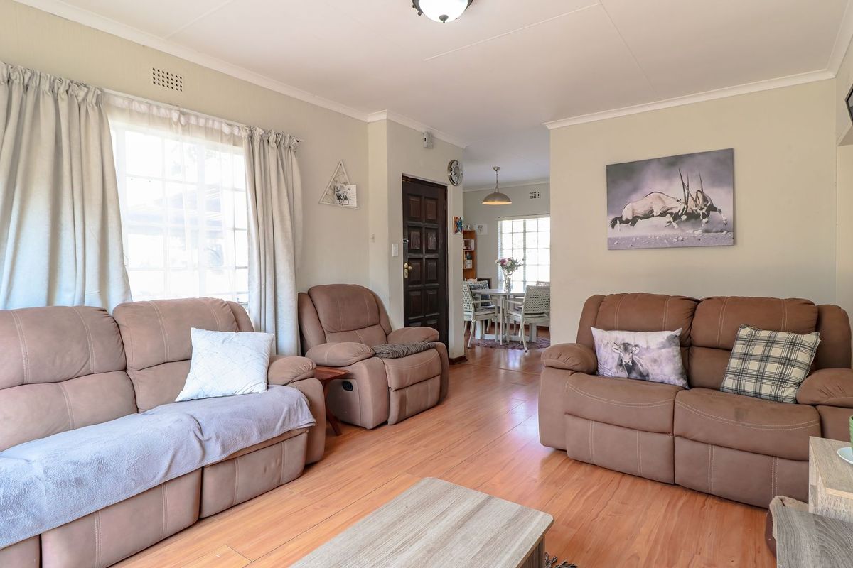 A comfortable living room featuring laminate flooring, coving, and a timber front door, with an open flow leading through to the dining area.