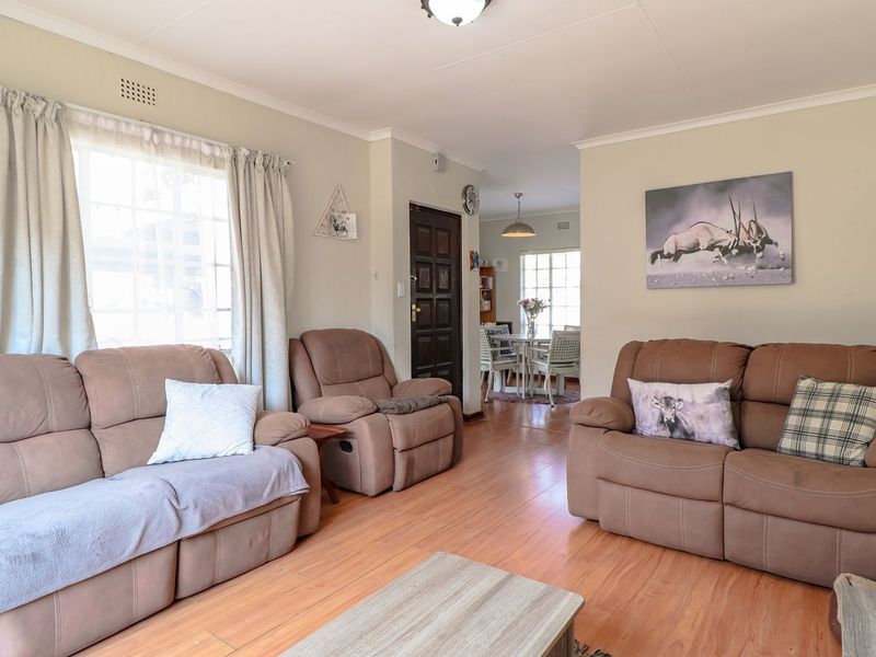 A comfortable living room featuring laminate flooring, coving, and a timber front door, with an open flow leading through to the dining area.