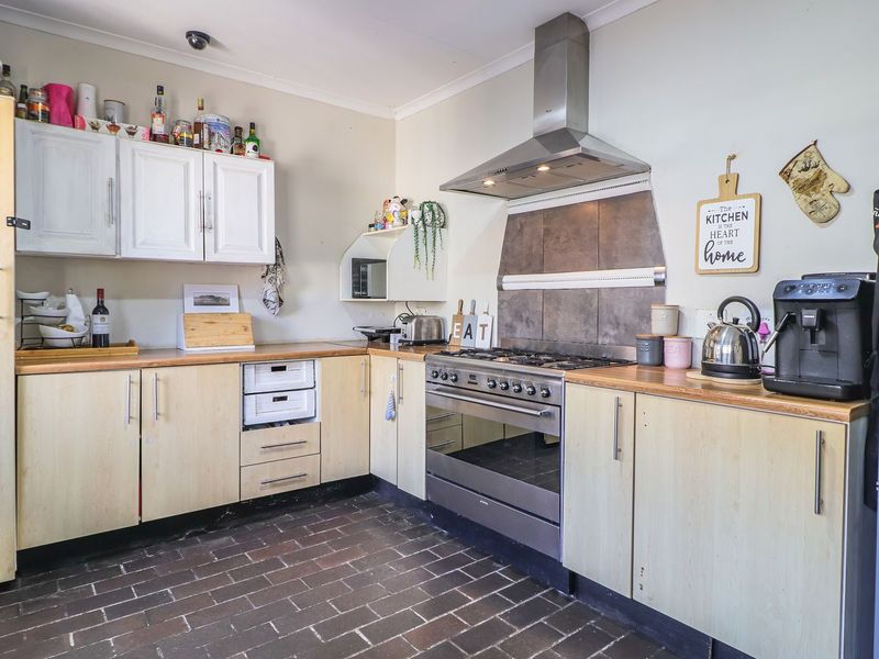 A functional kitchen featuring light wood cabinetry, laminate countertops, a stainless steel gas stove with extractor fan, and durable brick flooring.