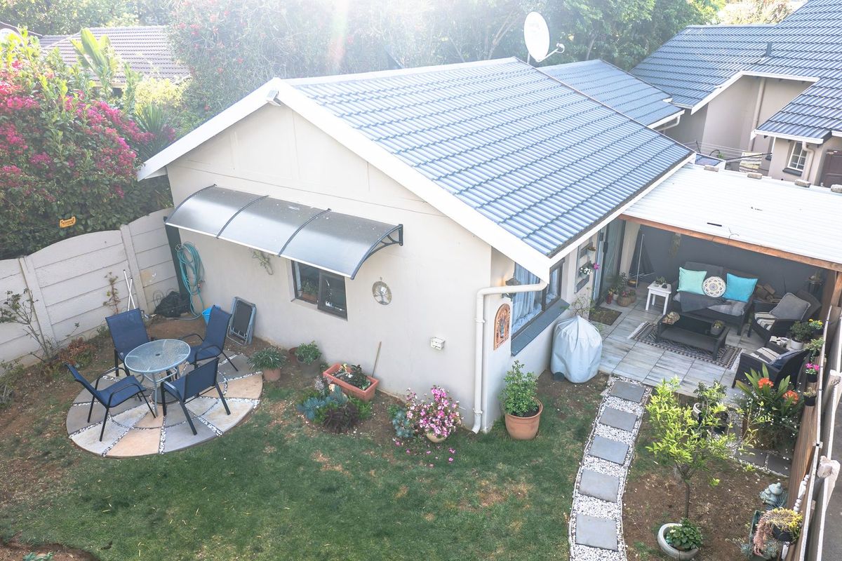 Aerial view of a rear garden featuring a covered patio, paved walkway, and a well-maintained tiled roof structure.