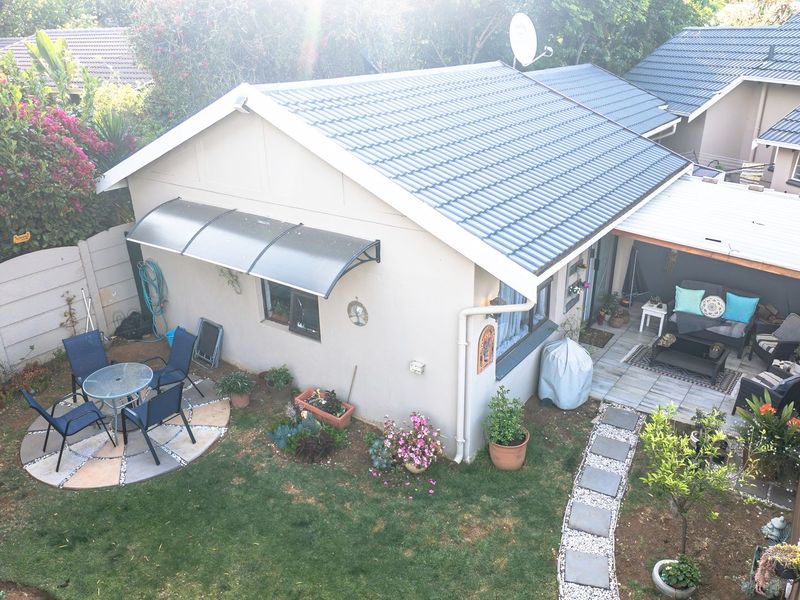 Aerial view of a rear garden featuring a covered patio, paved walkway, and a well-maintained tiled roof structure.
