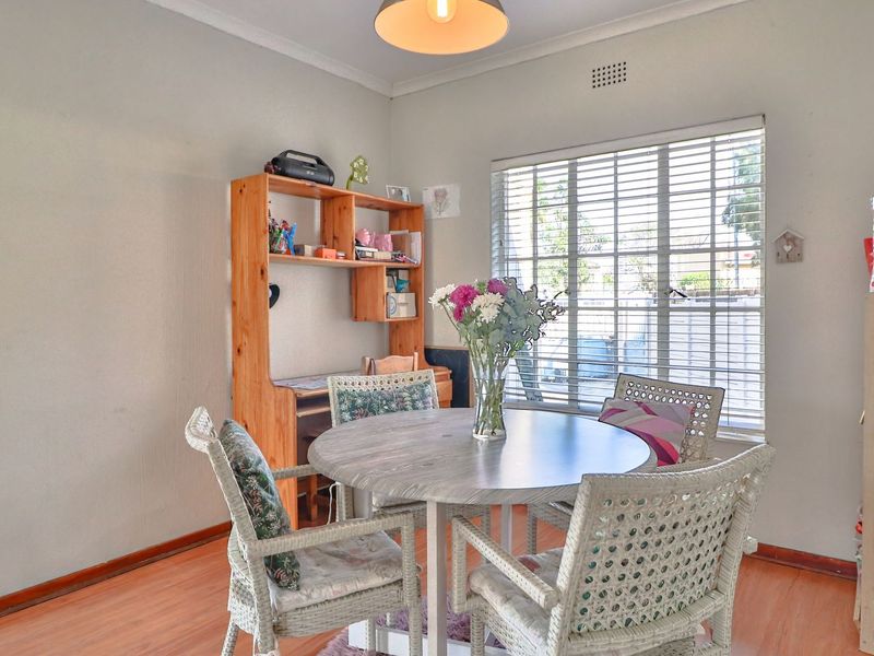 A bright dining area featuring laminate flooring, neutral walls, and large windows with fitted venetian blinds, providing a functional space for meals.