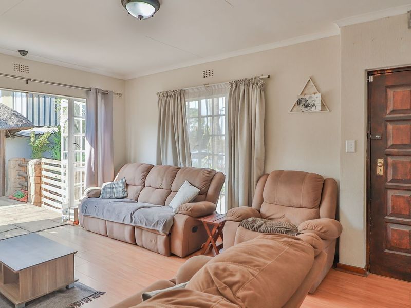 A living room featuring laminate flooring, a timber panelled entrance door, and a sliding glass door providing access to an outdoor patio area.