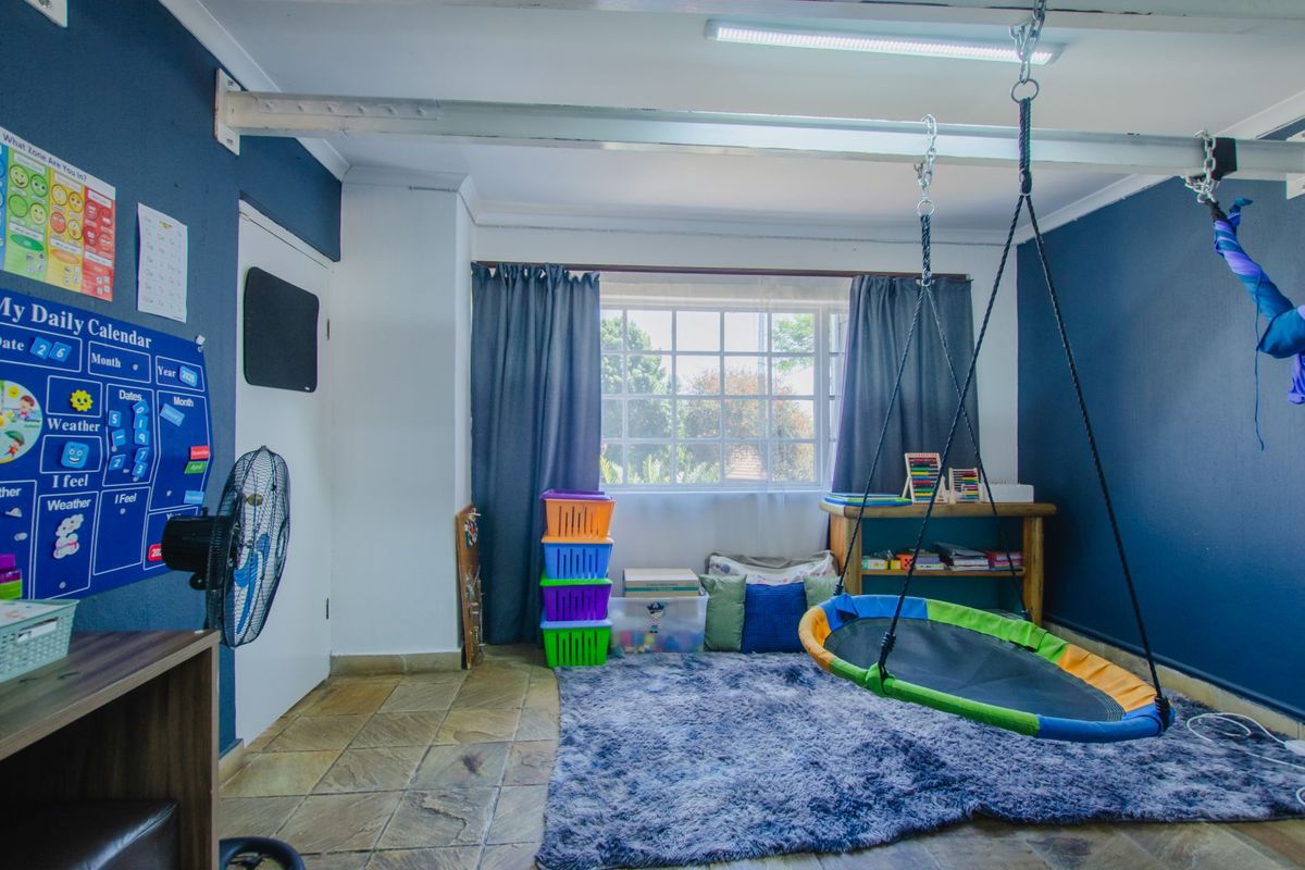 A versatile room featuring tiled flooring, dark blue accent walls, and a ceiling-mounted support beam, currently utilized as a play area.