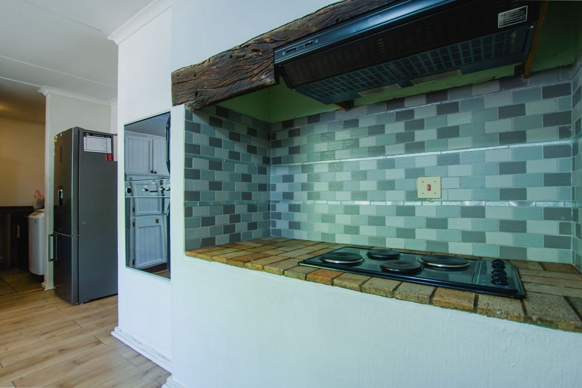 Kitchen area featuring a built-in electric hob, tiled countertop, decorative timber beam mantle, and a tiled backsplash with an integrated extractor fan.