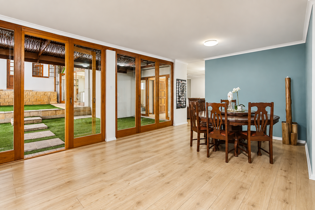 Spacious living area featuring light-toned laminate flooring and extensive timber-framed sliding glass doors providing seamless access to the outdoor patio and garden area.