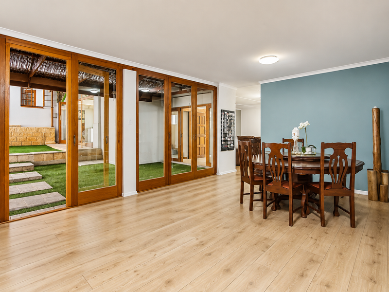 Spacious living area featuring light-toned laminate flooring and extensive timber-framed sliding glass doors providing seamless access to the outdoor patio and garden area.