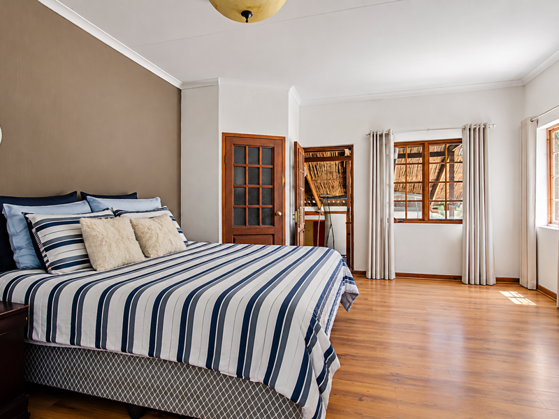 A spacious bedroom featuring warm laminate flooring, neutral wall tones, and natural light through wooden-framed windows, offering a comfortable and inviting atmosphere.