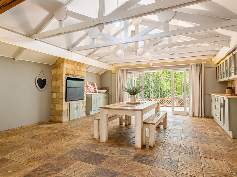 Spacious open-plan living and dining area featuring exposed vaulted timber trusses, a stone fireplace, and direct access to an outdoor patio through sliding doors.